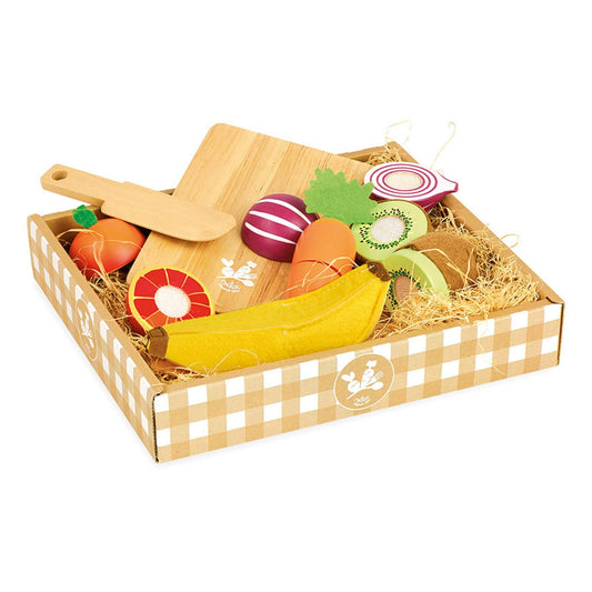 A cardboard tray filled with wooden play food including a banana, orange, onion, kiwi, carrot, chopping board, and toy knife on a straw-like base.