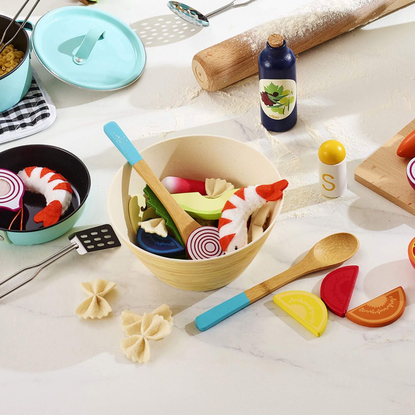 Wooden salad play set in kitchen play scene with rolling pin, toy vegetables, wooden utensils and pretend cooking accessories.