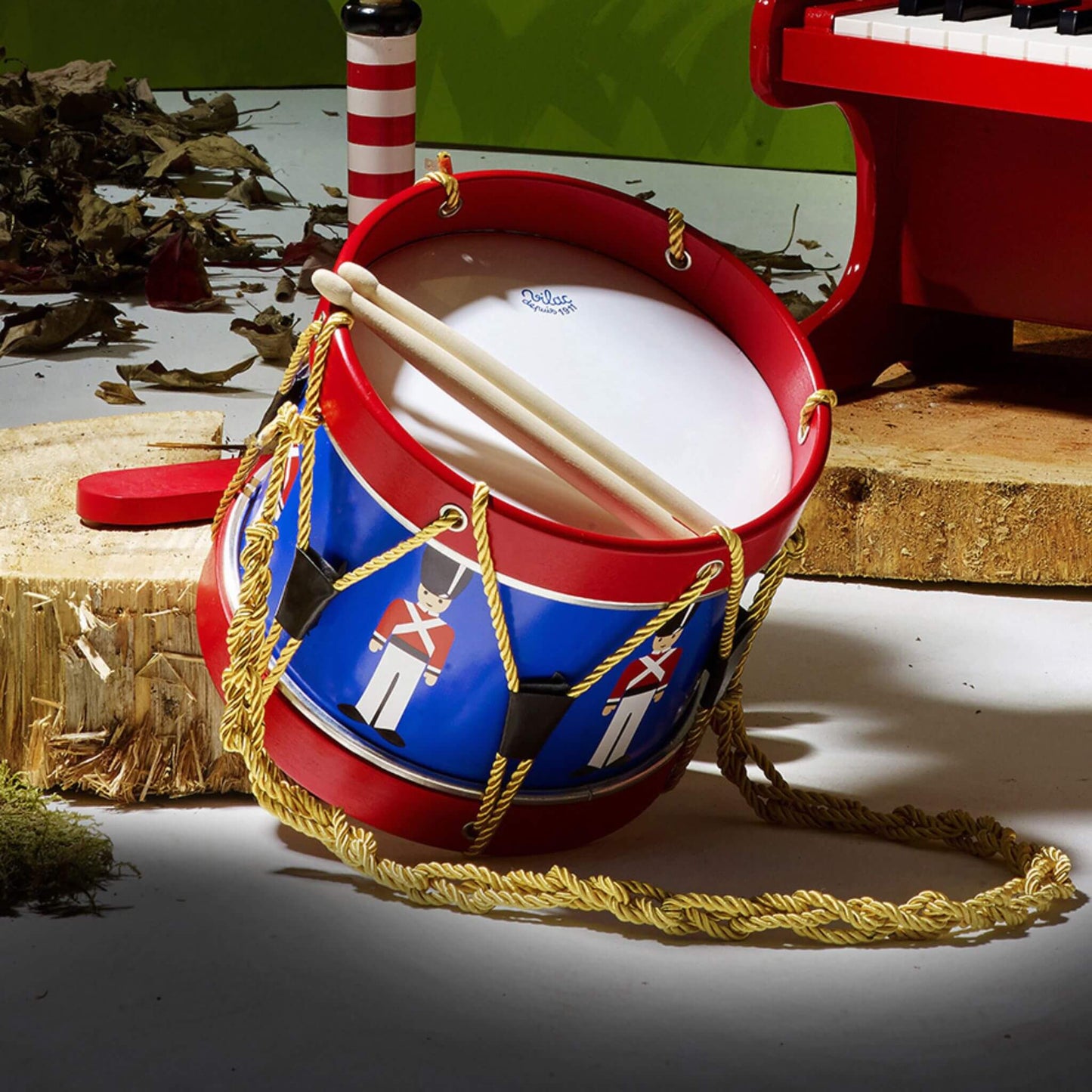 Wooden toy drum with soldier illustrations displayed in a play setting next to a toy piano, showcasing musical toys for children.