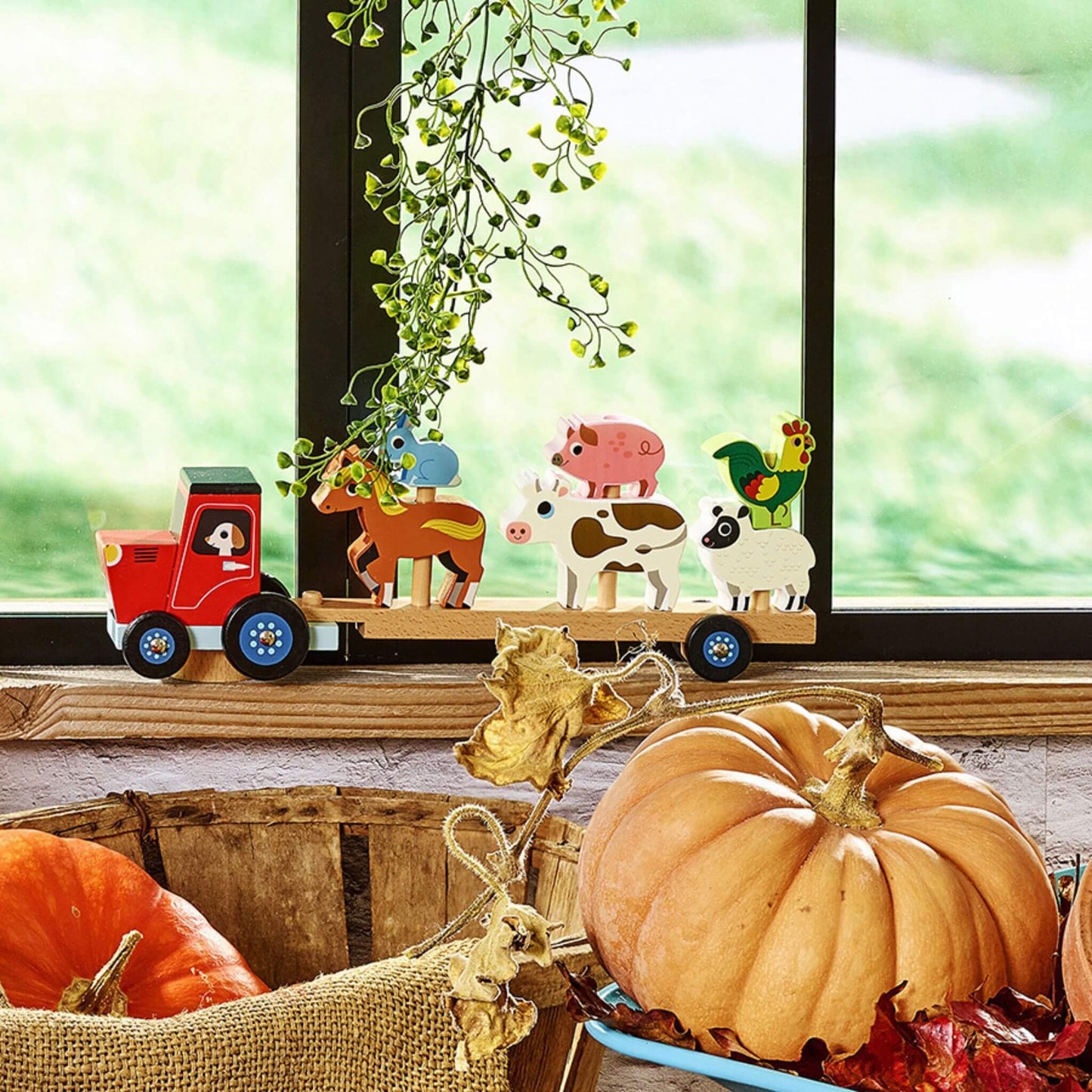 Toy wooden tractor and farm animal set displayed on windowsill with autumn pumpkins, creating a seasonal harvest play scene.