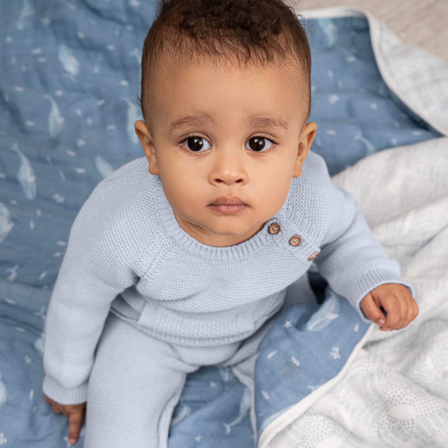 Baby sitting on the aden + anais organic muslin blanket in Oceanic whale print. Blanket is soft, durable, and gentle on delicate skin.