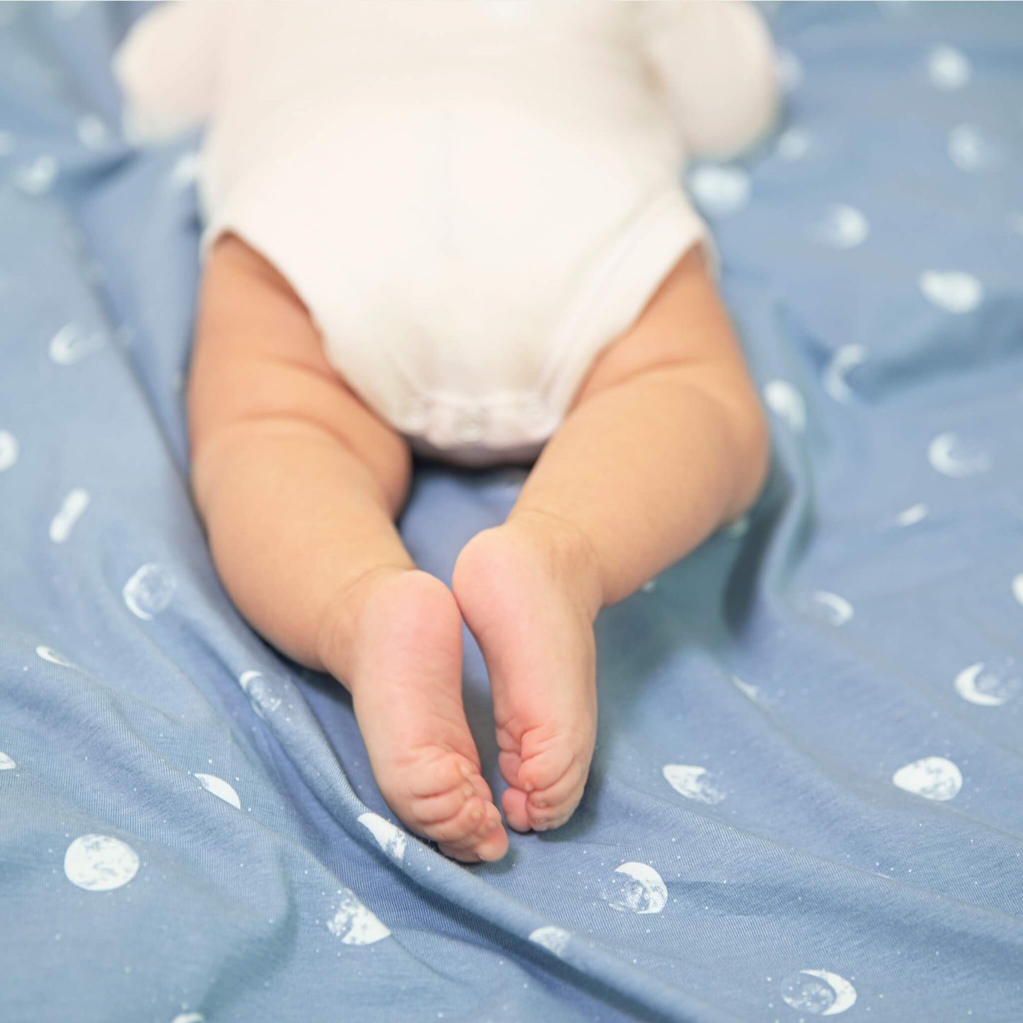 Close-up of baby’s feet lying on the Blue Moon swaddle blanket by aden + anais. Shows soft texture and print.