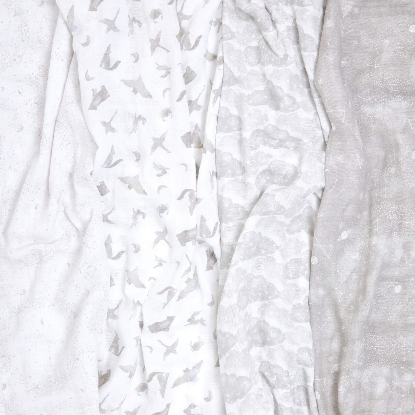 Overhead view of four crumpled aden + anais muslin swaddles in soft grey celestial prints. Organic cotton baby blankets designed for everyday use.