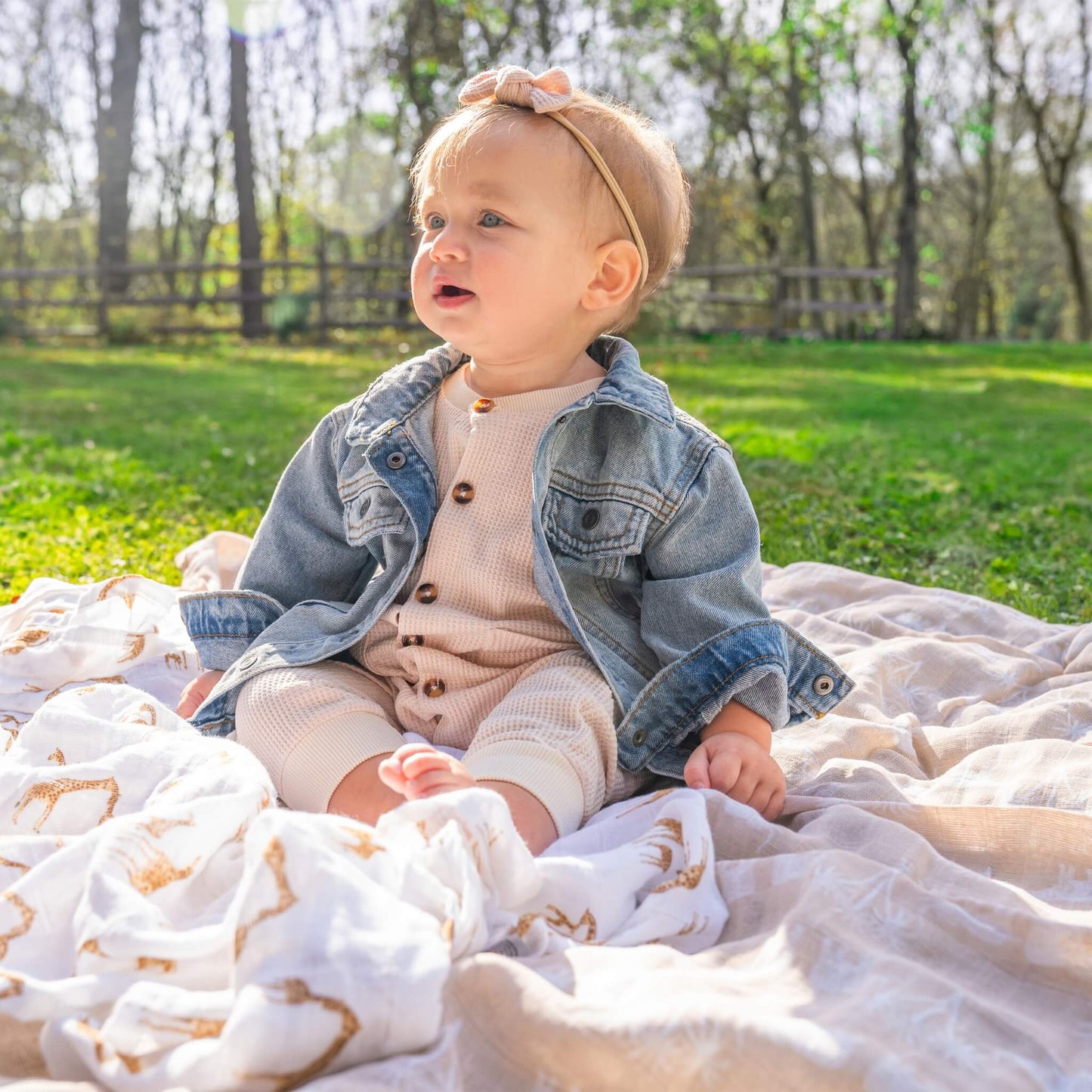 Baby seated outdoors on layered aden + anais Safari Dreams swaddles, showing giraffe and palm tree prints in warm, earthy hues.