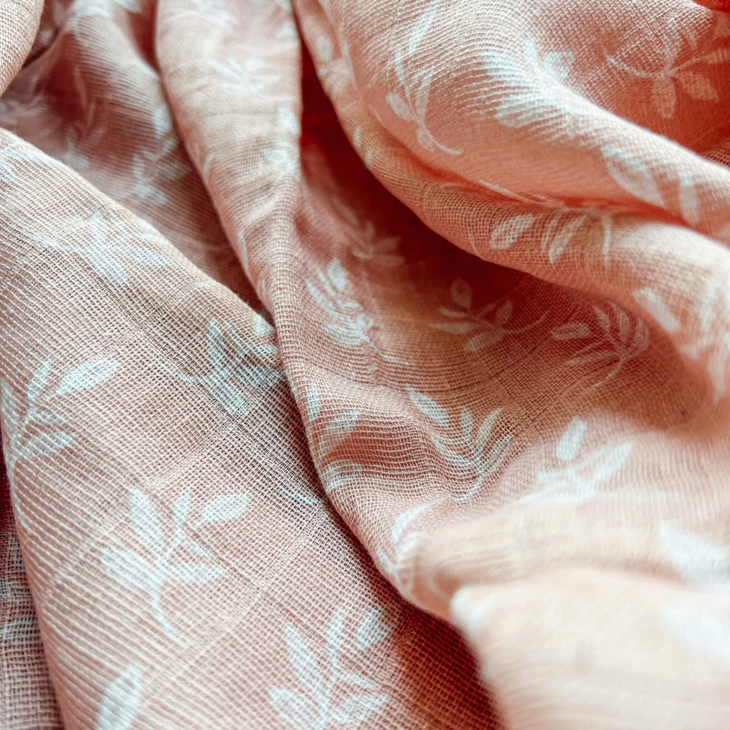 Close-up of aden + anais Earthly swaddle in pink. Soft organic muslin fabric with delicate white leaf design and airy weave.