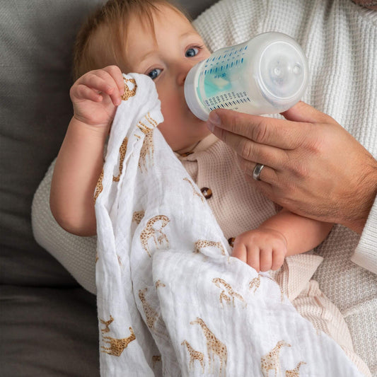 Baby holding an Aden + Anais organic muslin square in Safari Dreams print while being bottle-fed, showcasing soft, breathable fabric.