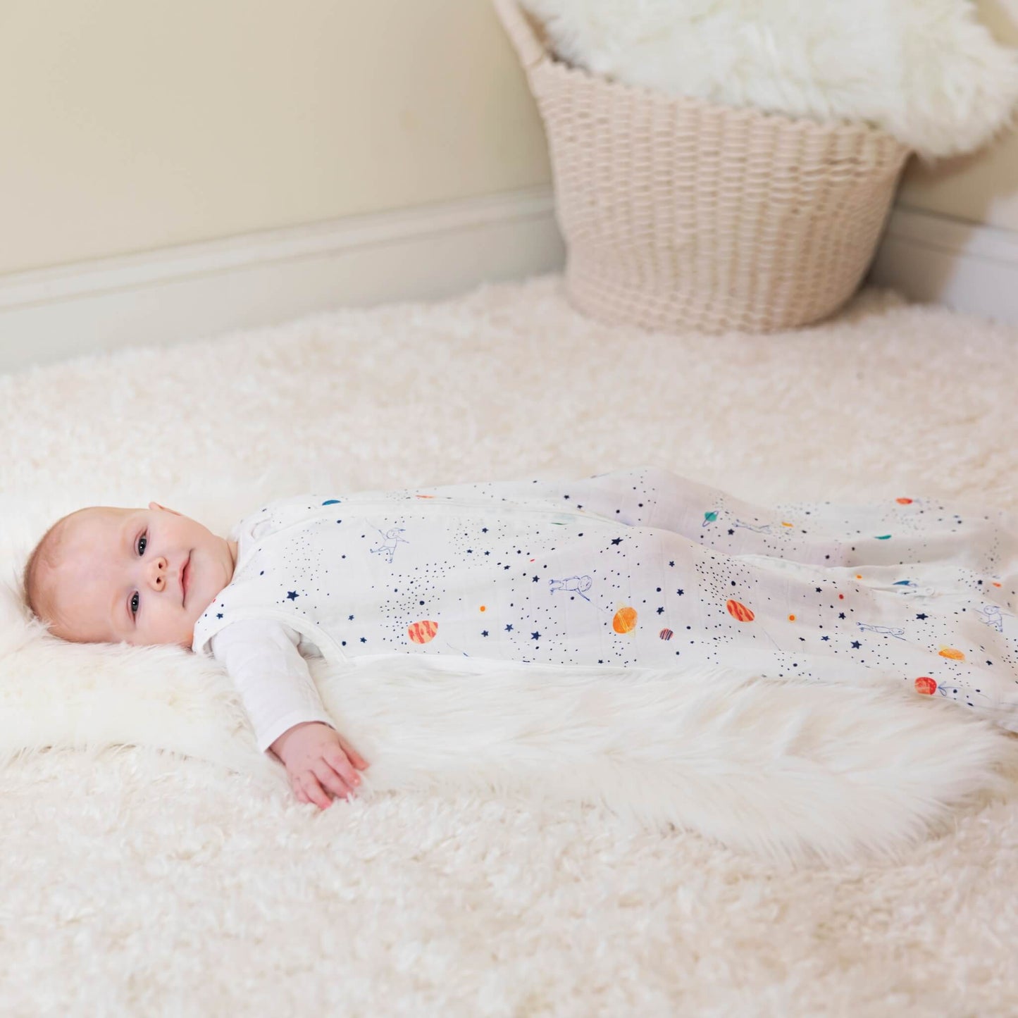 Baby lying in cot wearing aden + anais Stargaze sleeping bag. 1.0 TOG muslin sleep sack in breathable bamboo fabric with space-themed print.