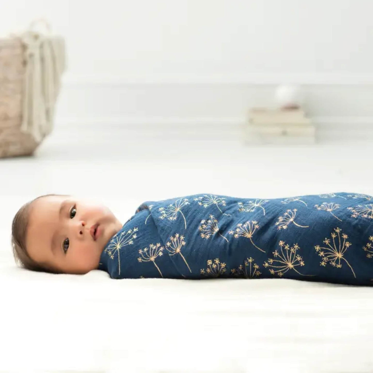 Baby comfortably swaddled in aden + anais muslin swaddle with a navy floral design and gold accents.