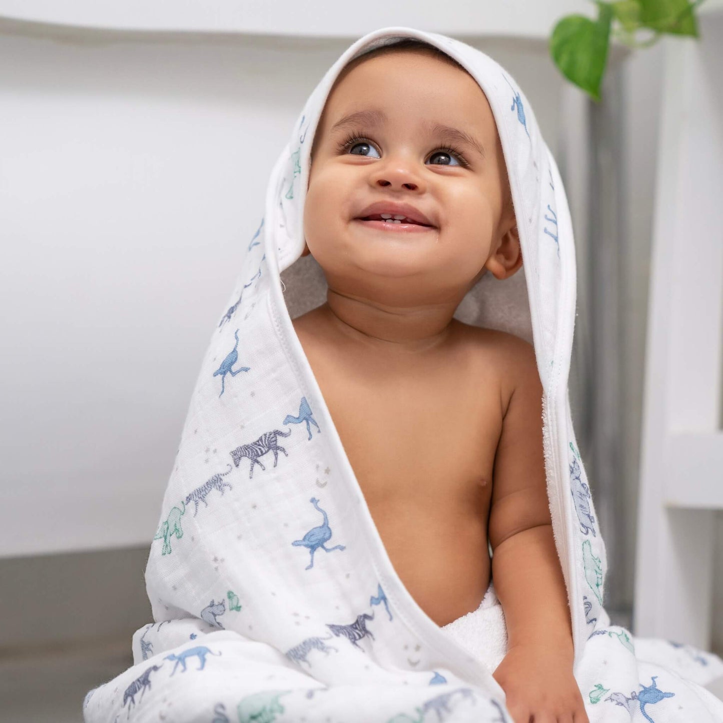 Smiling baby wrapped in aden + anais Rising Star hooded towel. Soft muslin hood with blue safari animal print.