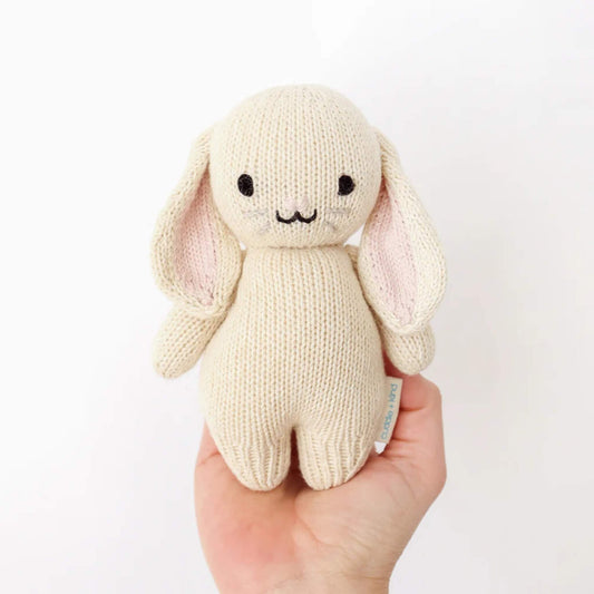 A small knitted bunny soft toy held in an adult hand showing scale and size for babies.