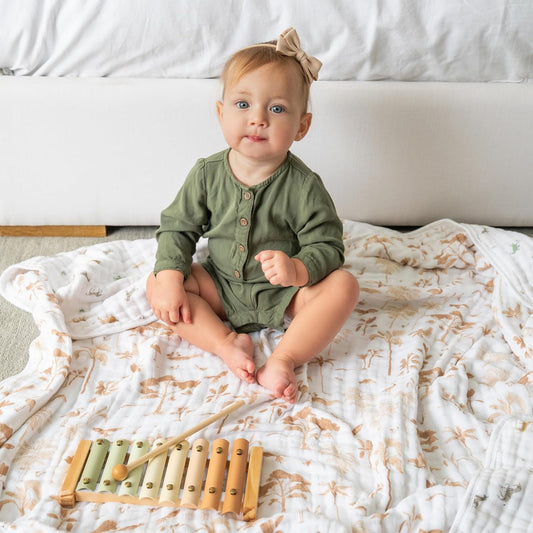 Baby sitting on the aden + anais Safari Dream organic muslin blanket. Soft and breathable, with a subtle safari animal and palm tree print.