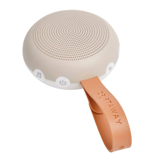 Close-up of a small, round taupe portable sound machine with perforated speaker holes on top and a looped orange strap embossed with the word Drift Away.
