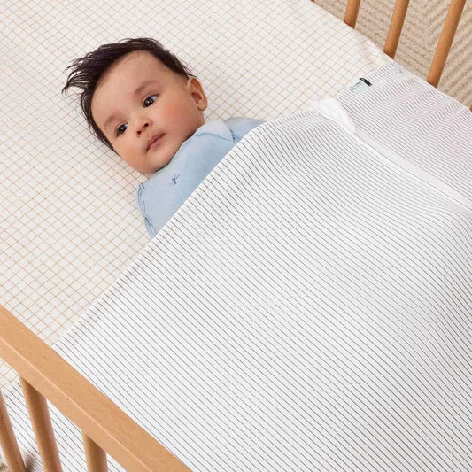 Baby lying under the HugMe Blanket in midnight stripe, showing the secure fit across the cot mattress.
