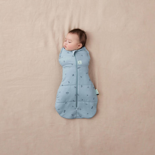 Baby wrapped snugly in a blue Winter Cocoon Swaddle Bag with dragonflies print, zip-up front, and bell-shaped bottom.