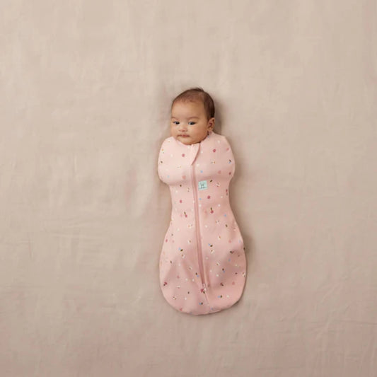 Newborn baby lying on a neutral surface wrapped in a pink Cocoon Swaddle Bag with daisy and ladybird print, arms fully swaddled inside.
