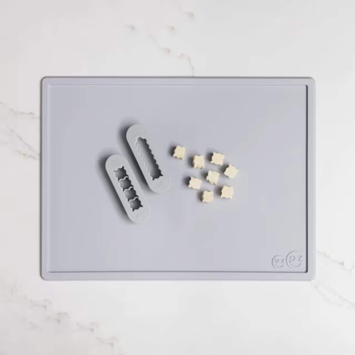 Grey silicone food cutters beside small cubes of soft food prepared for baby finger foods on a matching placemat.