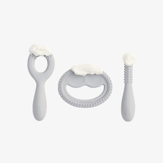Three grey silicone oral development tools shown with soft food puree placed on textured chewing surfaces to demonstrate use for early feeding practice.