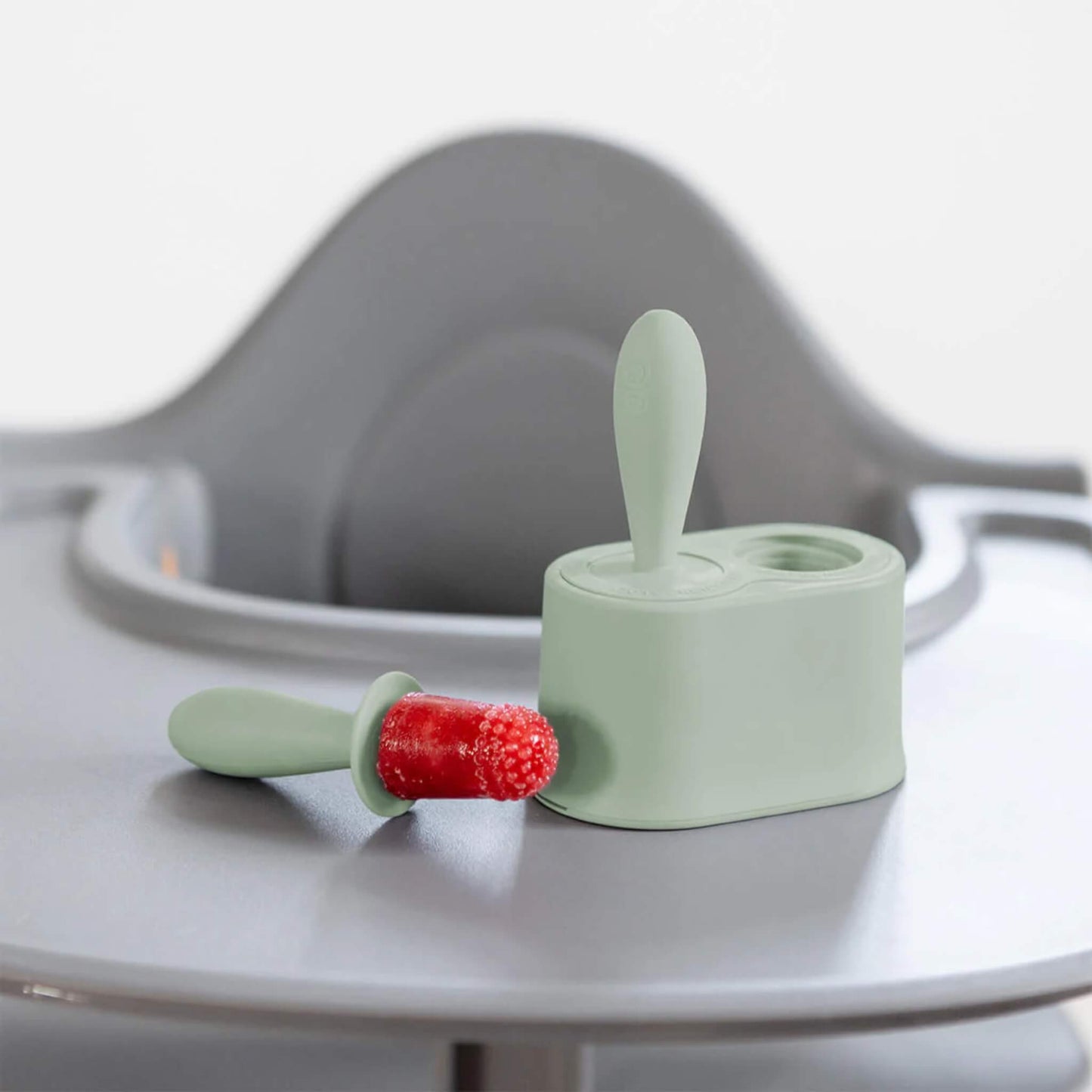 Frozen fruit baby popsicle with textured silicone tip resting beside baby popsicle mould base on a highchair tray.