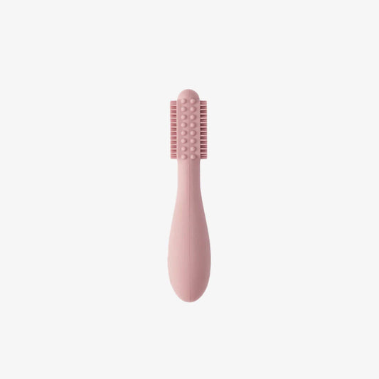 Blush pink silicone baby toothbrush showing soft bristles on both sides with raised sensory bumps along a rounded head and a thick easy-grip handle for small hands.