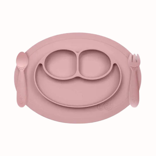 Silicone divided mini mat in blush with matching spoon and fork placed on either side for toddler self-feeding.