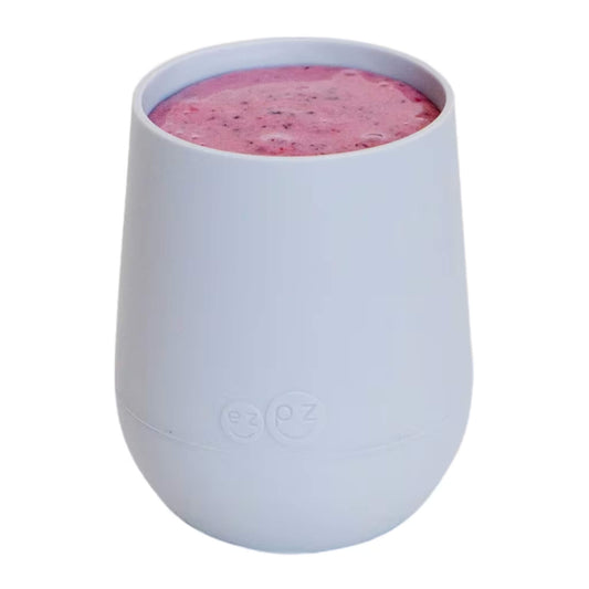 A pewter silicone training cup shown filled with milk, designed for toddlers learning to drink from an open cup.