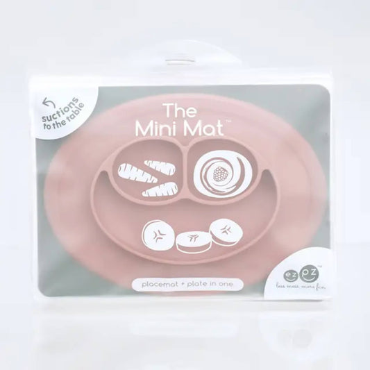 A suction placemat and plate in blush pink silicone with food compartments , placed inside retail packaging.