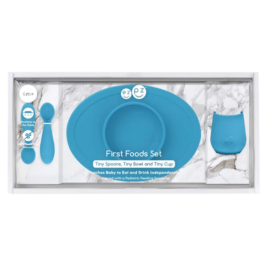 Boxed baby feeding set in blue showing a suction bowl, open cup and training spoons inside clear retail packaging with product details.