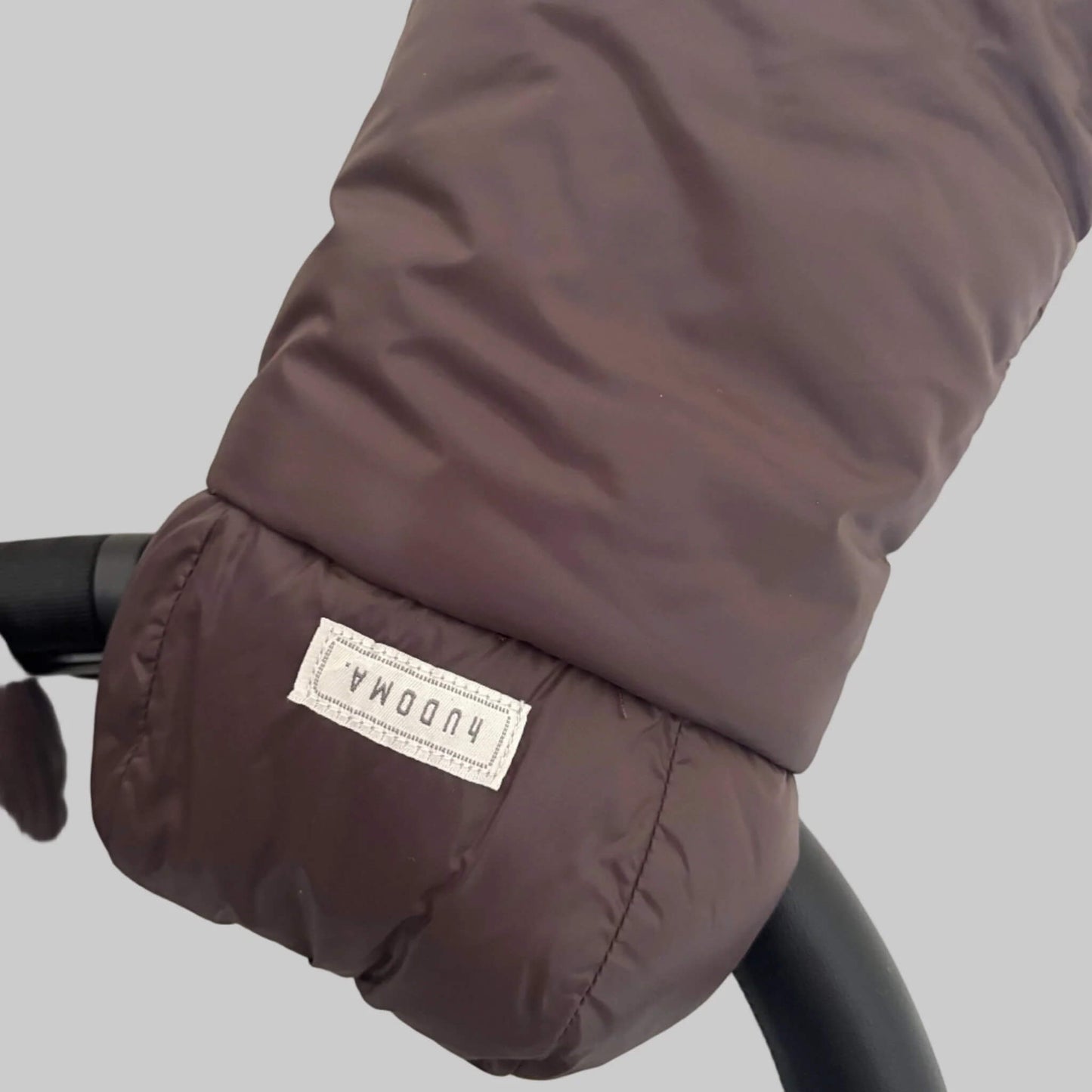Detailed view of brown pram glove exterior fabric and hUDOMA brand label on the side of the stroller handle.