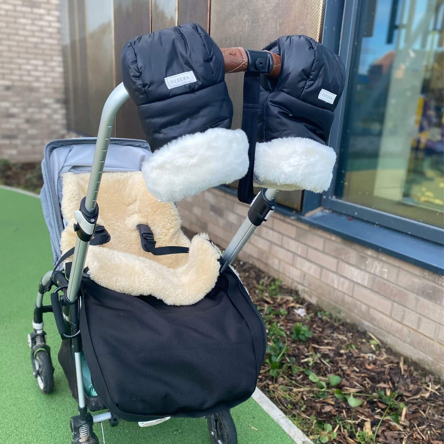 Outdoor lifestyle image of a stroller featuring Pram Gloves securely attached to the handle, showcasing their sleek black design with soft white faux fur lining, paired with a cosy sheepskin liner, ideal for cold-weather strolls.