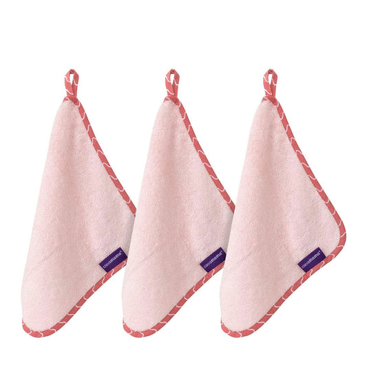 Three pink bamboo washcloths hanging by their corner loops, showing the soft terry texture and coral-trimmed edging.