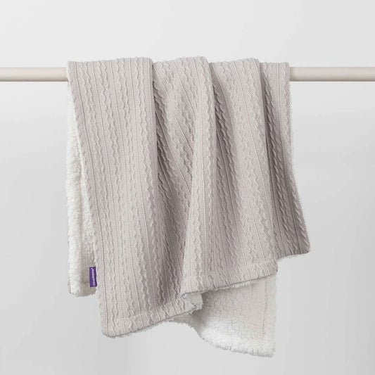 Grey cable-knit baby blanket with sherpa fleece reverse, draped over a white rail to show both textures.