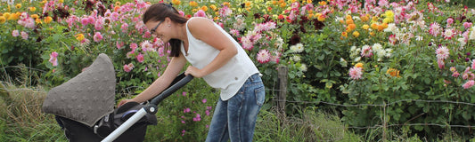 Woman pushing a pram along a garden path surrounded by blooming flowers.