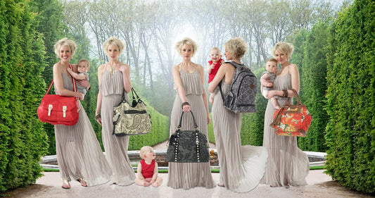Women standing outdoors with babies and changing bags, gathered together between tall green hedges.