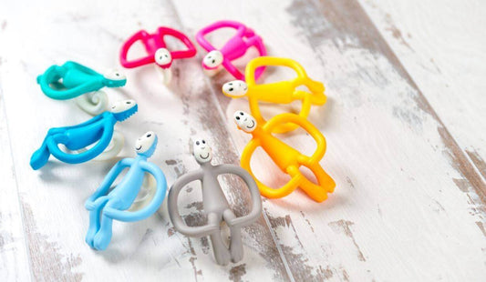 Colourful silicone baby teethers arranged in a circle on a wooden surface.