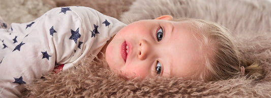 Child lying on a soft sheepskin rug, featured in a Bebeco article about Naturally Sheepskins.