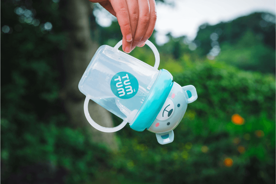 Hand holding a blue Tum Tum training cup outdoors.
