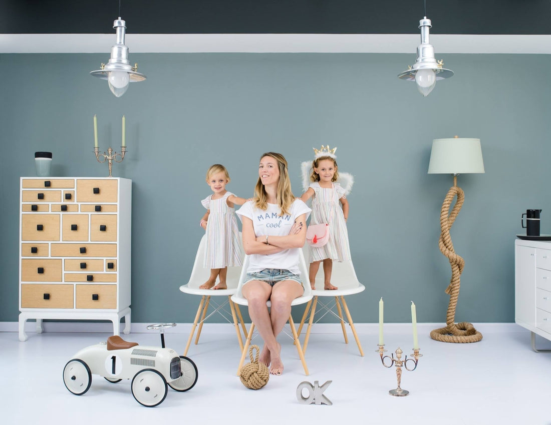 Three children and two adults sitting together in a playroom with wooden ride-on toys, storage units, and decorative lighting against a pale blue wall.