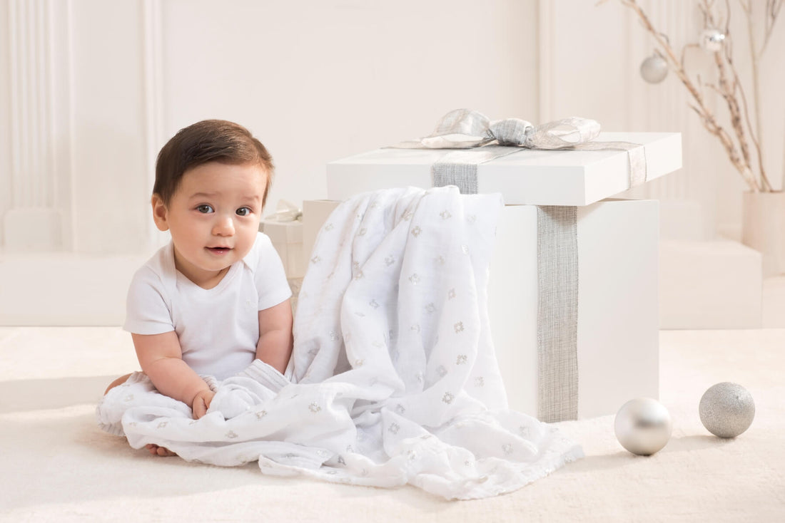 Baby sitting on a soft play mat reaching for a textured grey blanket next to a low white table.