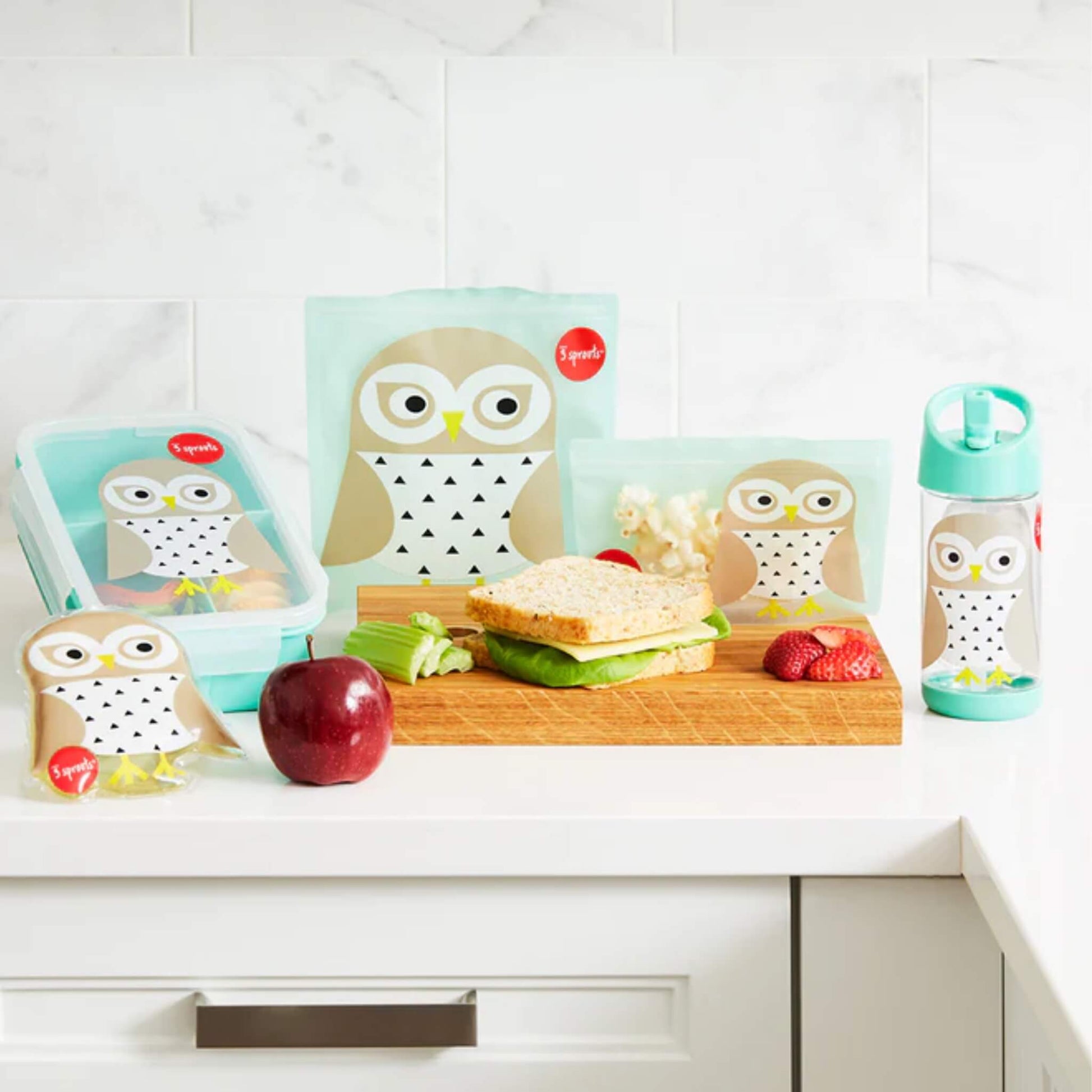 3 Sprouts Owl lunch range on a kitchen counter, featuring the sandwich bag, snack bag, bottle, and lunchbox with food.