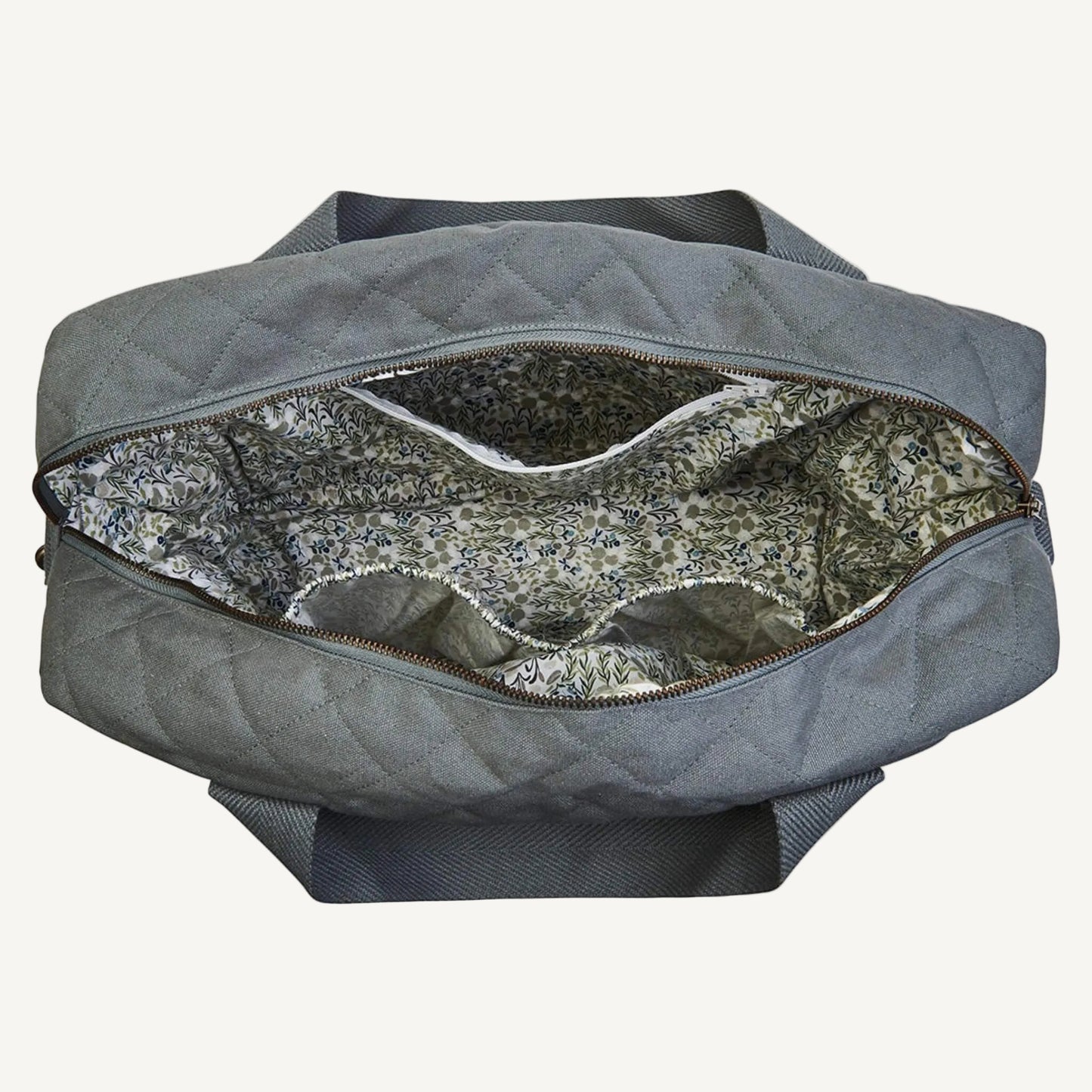 A grey quilted canvas baby changing bag opened to show a floral cotton lining, internal elasticated pockets and a central zip pocket.