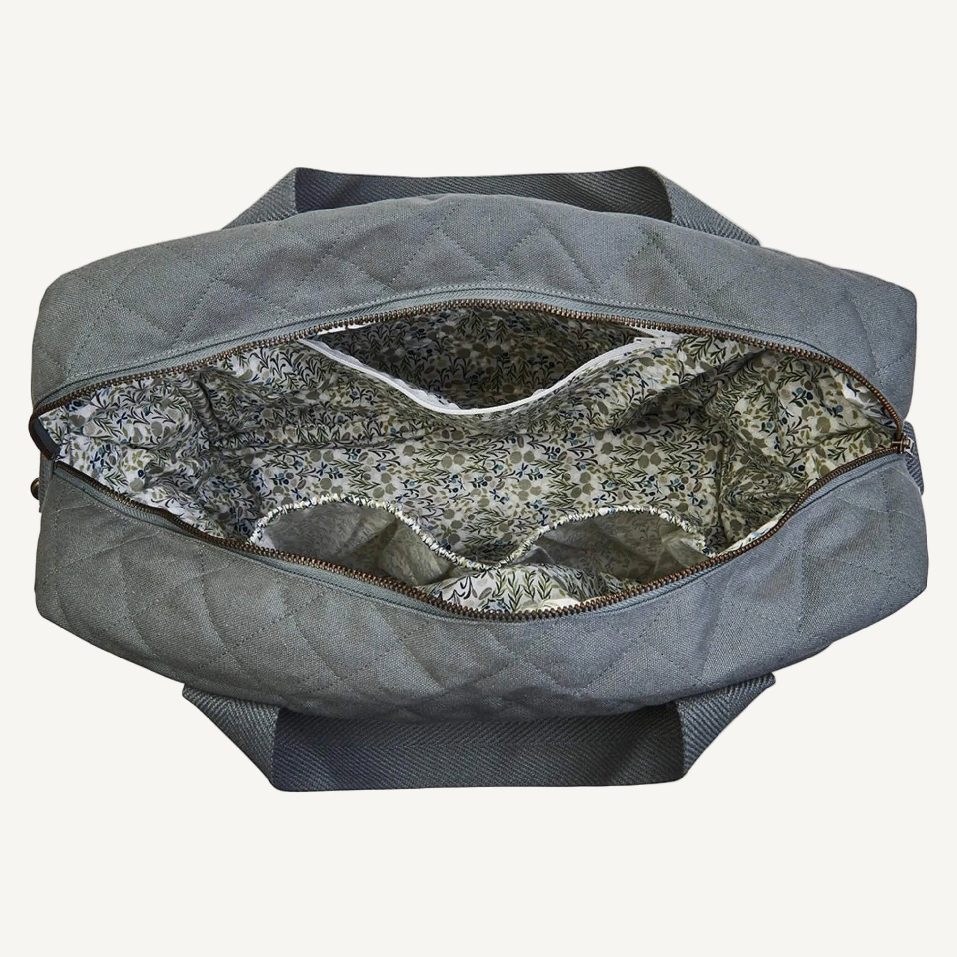 A grey quilted canvas baby changing bag opened to show a floral cotton lining, internal elasticated pockets and a central zip pocket.