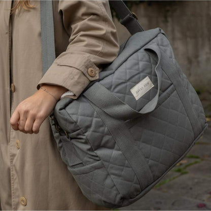 A quilted grey canvas baby changing bag carried on the shoulder, showing padded structure, stitched detailing and sturdy woven handles.