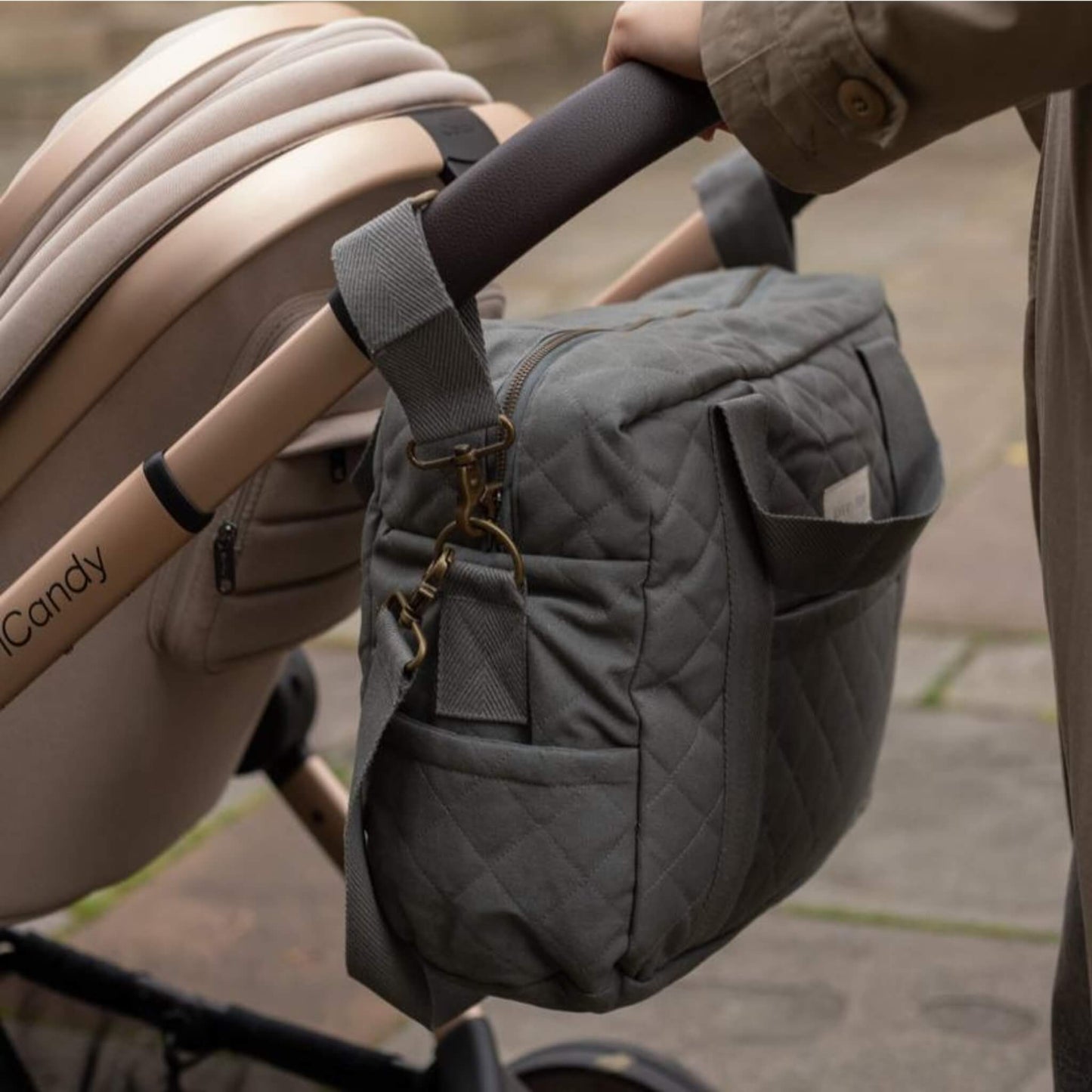 A quilted grey canvas baby changing bag attached to a pushchair handle using fabric pram clips for hands free use.