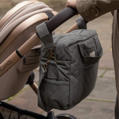 A quilted grey canvas baby changing bag attached to a pushchair handle using fabric pram clips for hands free use.