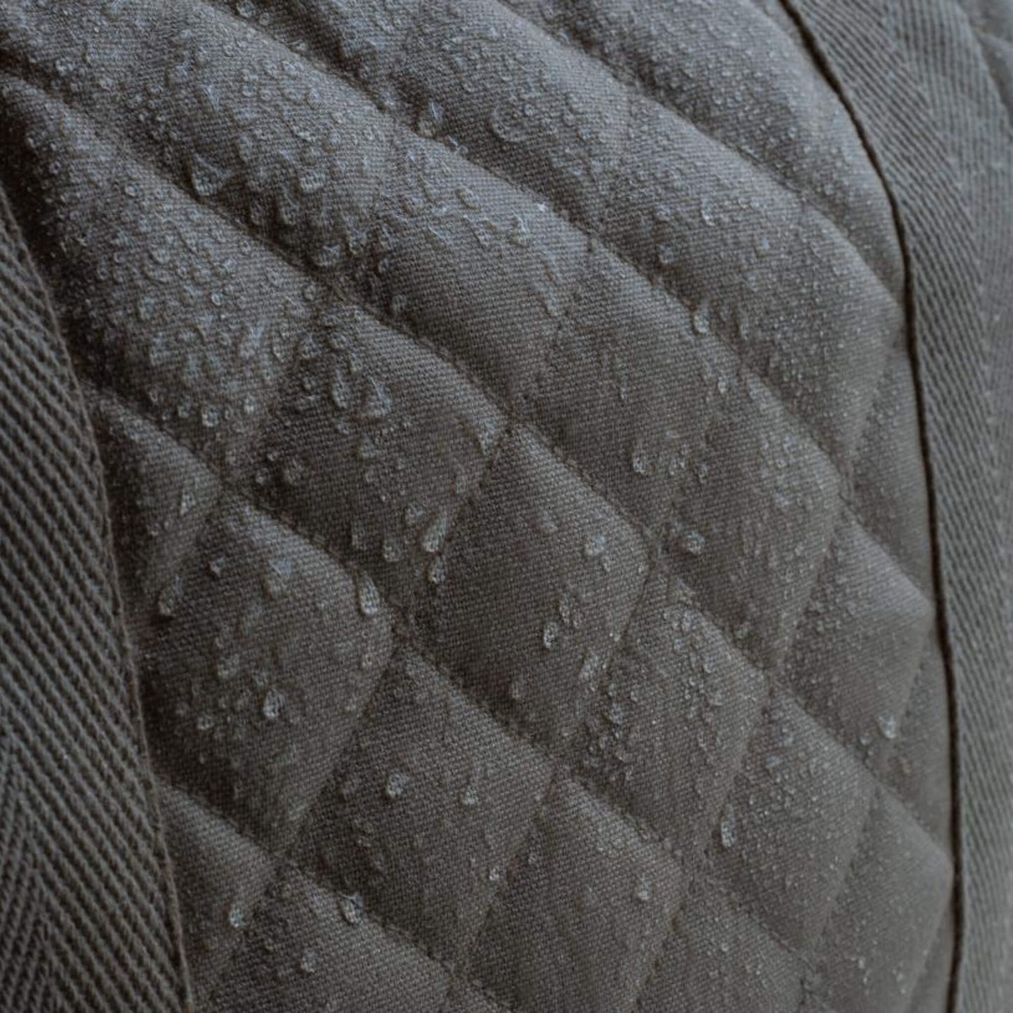 A close up of quilted grey canvas fabric with water droplets beading on the surface, showing a water resistant finish.