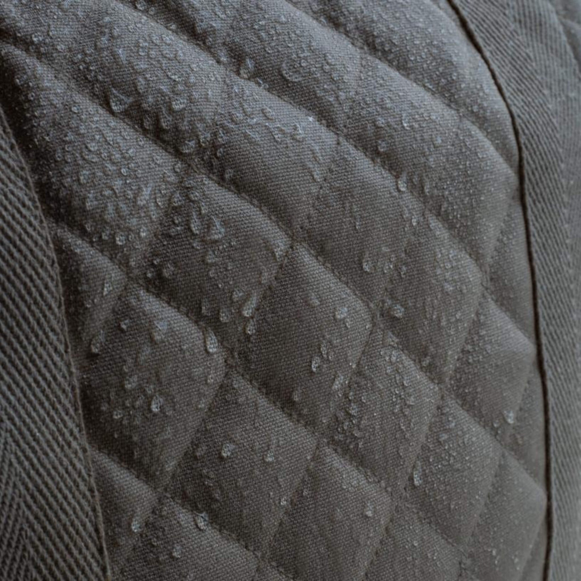 A close up of quilted grey canvas fabric with water droplets beading on the surface, showing a water resistant finish.