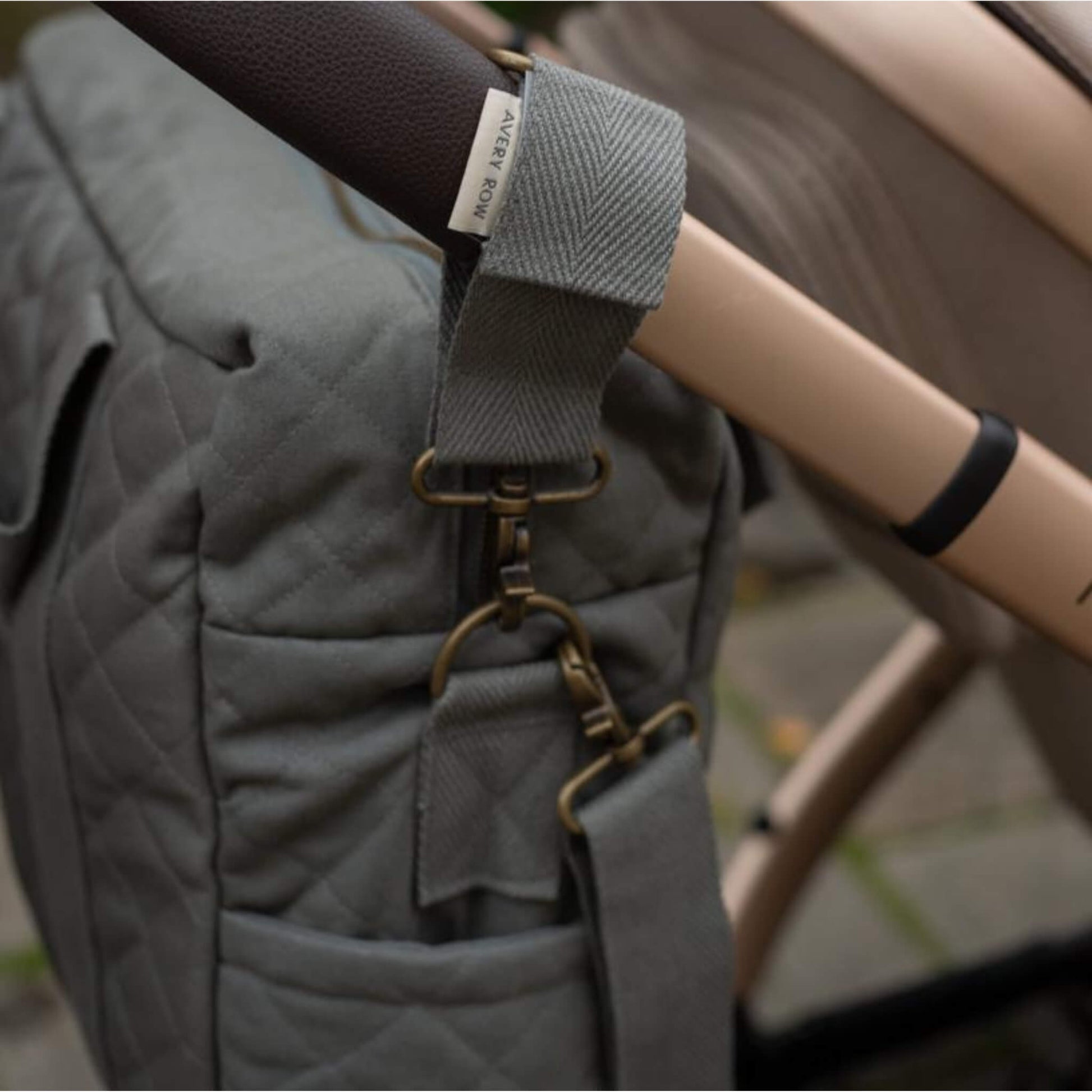 A close up of a fabric pram clip secured around a pushchair handle with metal fastening detail.