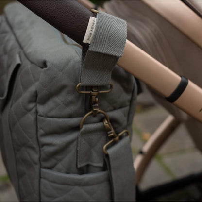 A close up of a fabric pram clip secured around a pushchair handle with metal fastening detail.