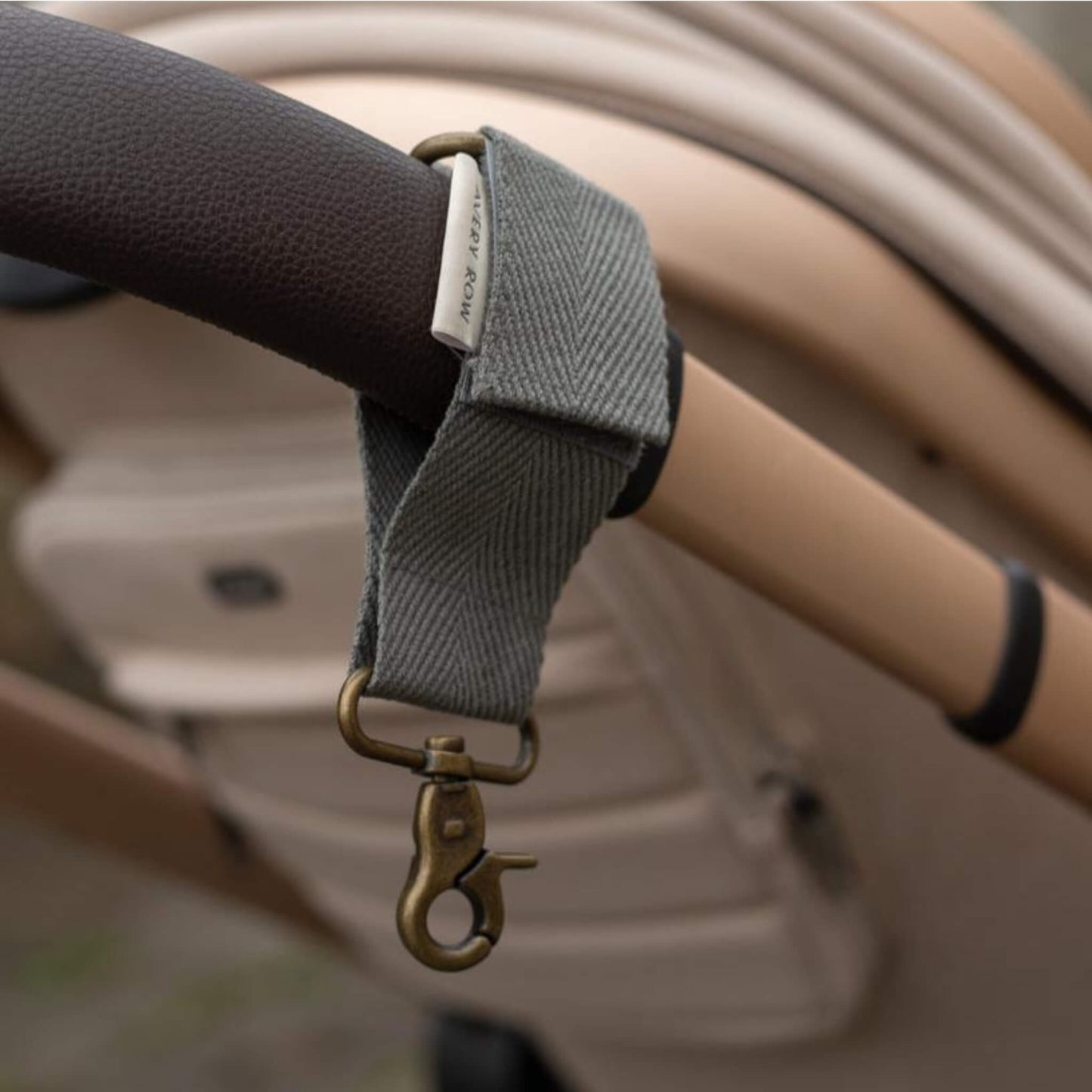 A fabric pram clip wrapped around a pushchair handle, showing woven texture and metal clasp attachment.