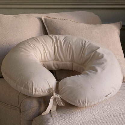 A cream nursing pillow with delicate chamomile print, displayed on a neutral armchair.